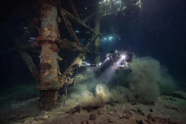 Underwater drone inspecting corroded steel jacket legs of a North Sea oil platform at 180 meters depth