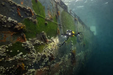 Underwater drone examining biofouling and marine growth on the hull of a large cargo vessel at anchor